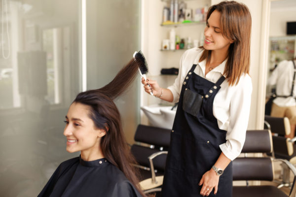 Hairdresser works with comb, female customer at the mirror in hairdressing salon. Stylist and client in hairsalon. Beauty business, professional service